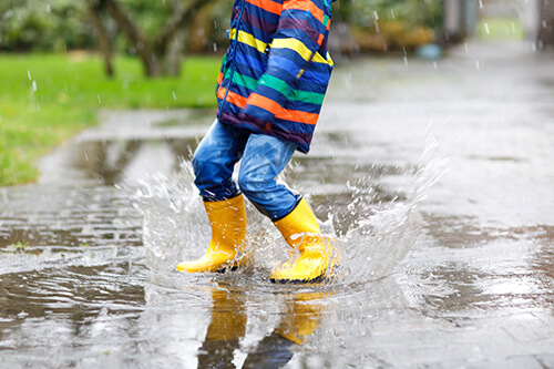 Child wearing boots splashing in water while it's raining