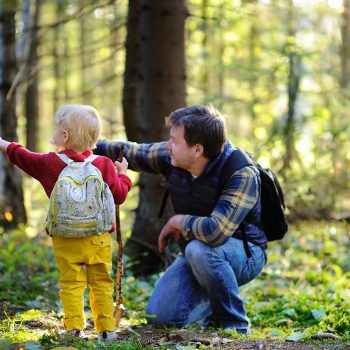 Parent and child outside in a forest wearing backpacks